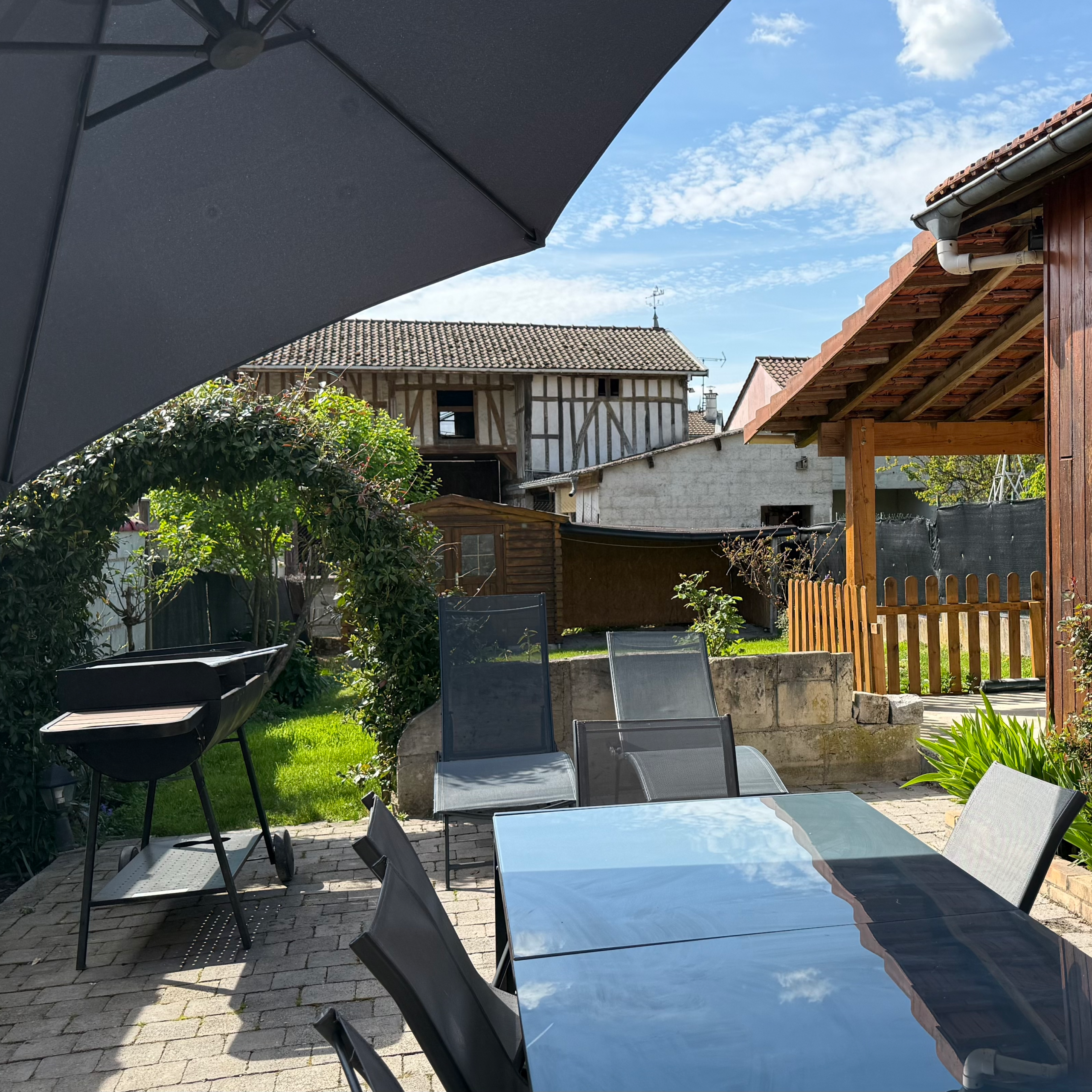 Extérieur du gîte avec salon de jardin, parasol et jeu de fléchettes